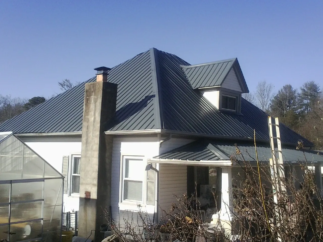 Dark blue standing seam metal roof on a white farmhouse with dormer — Slate & Tile Roof Repair by Roofing Brothers in Browder