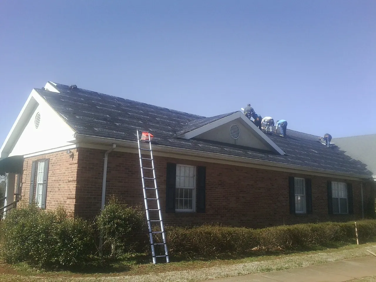 Crew tearing shingles off a brick ranch roof with a ladder set — Metal Roof Repair work by our crew in Browder