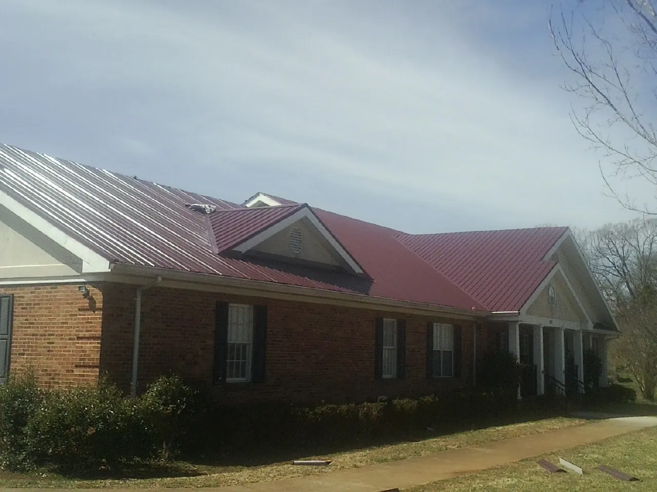 Red metal roof with gabled entries on a long brick building, from a Hail Damage Roof Repair job in Browder