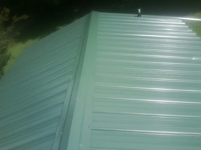 New green metal panels meeting at the ridge of a roof — Flat Roof Repair work by our crew in Browder