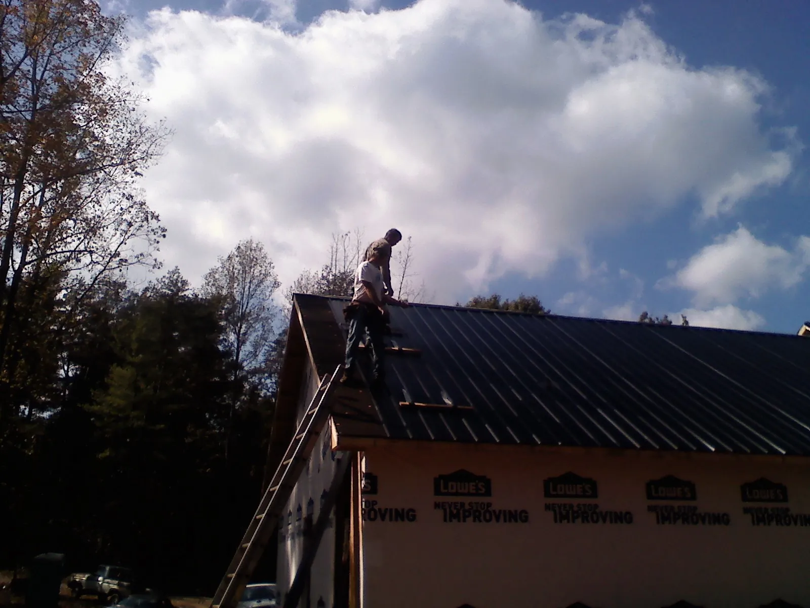 Roofer fastening dark metal panels high against a cloudy sky, from a Roof Inspection job in Browder