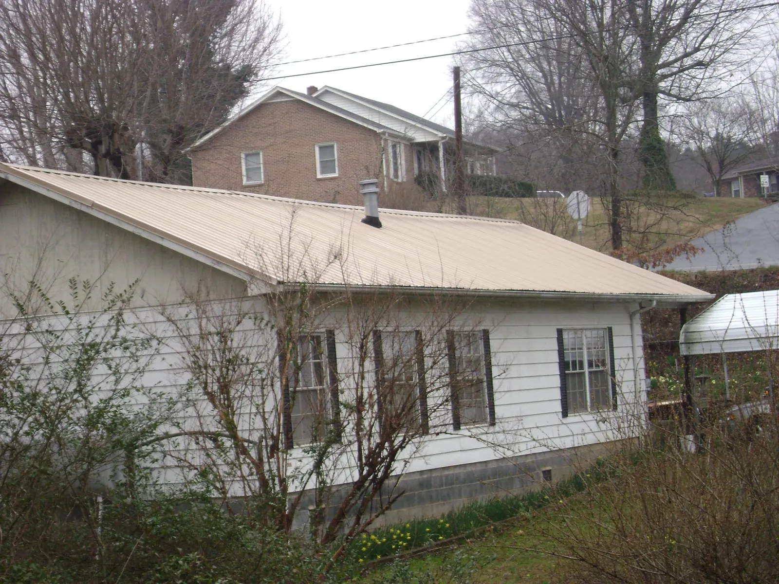 Tan metal roof on a white sided house set into a hillside — Commercial Roofing by Roofing Brothers in Browder